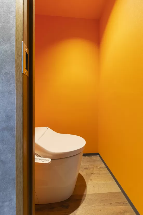 トイレのアクセントウォールにオレンジ色の壁紙クロスを使用した実例